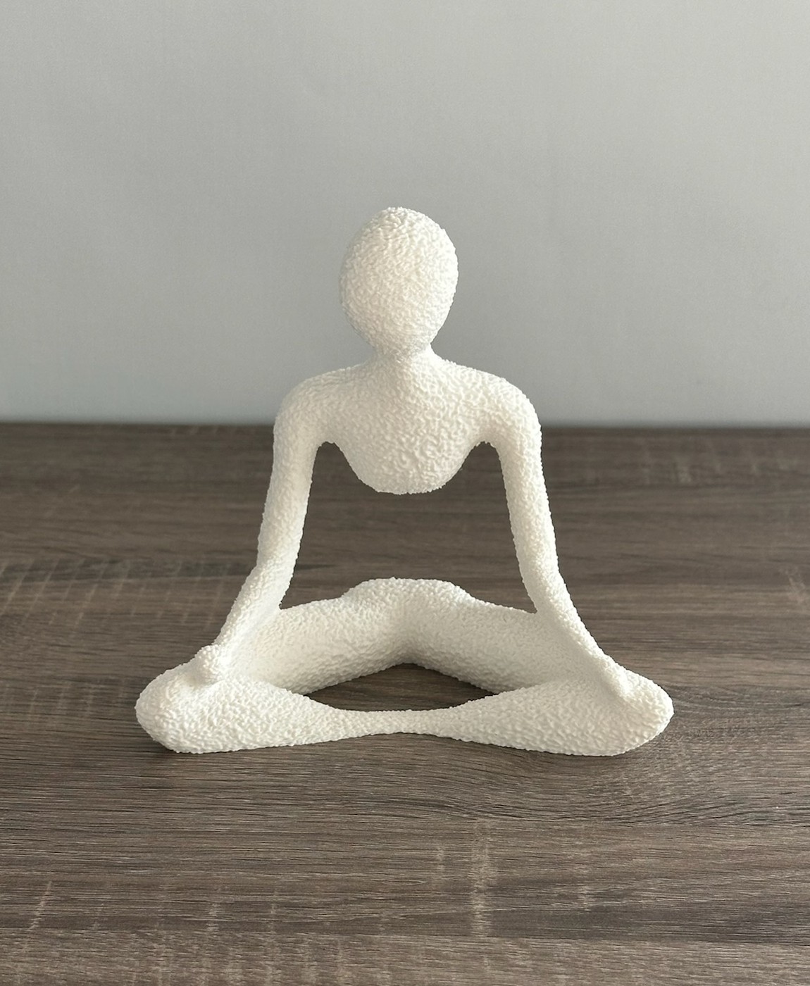 Estátua decorativa branca de figura humana em posição de ioga sobre mesa de madeira.