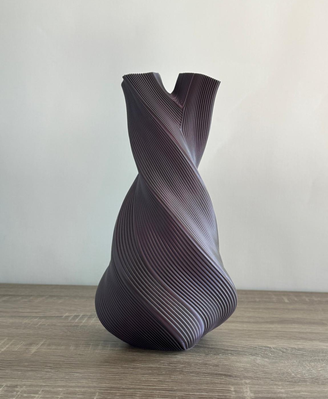 Vaso decorativo preto com textura em linhas torcidas sobre superfície de madeira.