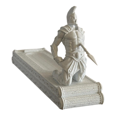 Estatueta de soldado espartano ajoelhado sobre base que parece um livro