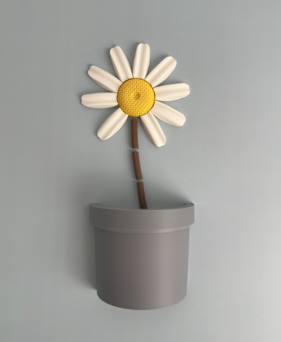 Vaso cinzento com flor decorativa branca e amarela num fundo cinzento.