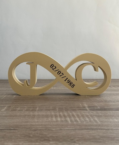 Estatueta dourada símbolo infinito com letras J e C e data 02/07/1988 sobre mesa de madeira