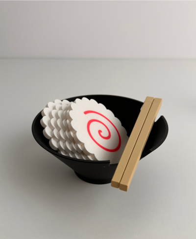 Taça preta com fatias brancas de peixe liofilizado e pauzinhos de madeira