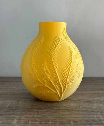 Vaso amarelo de cerâmica com folhas em relevo sobre mesa de madeira