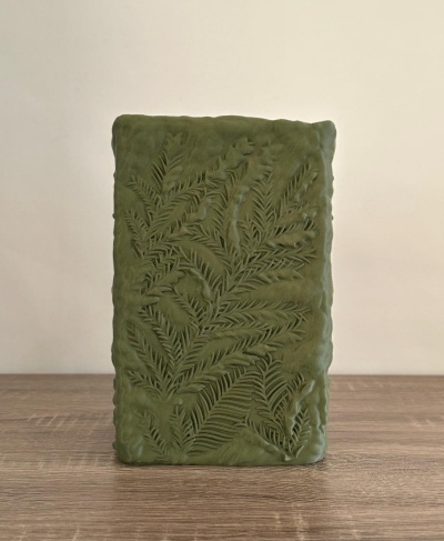 Vela decorativa verde com padrão de folhas e textura gravada