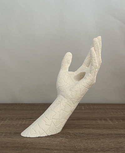 Escultura de mão branca com textura irregular sobre mesa de madeira