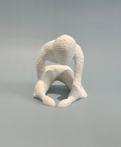 Escultura branca rugosa de figura humanoide agachada sobre fundo cinzento