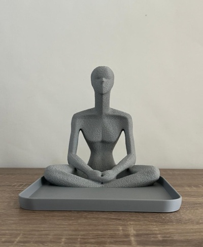 Estátua decorativa cinzenta de figura humana sentada em meditação numa bandeja cinzenta sobre madeira