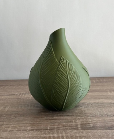 Vaso verde com padrão de folhas em relevo sobre mesa de madeira
