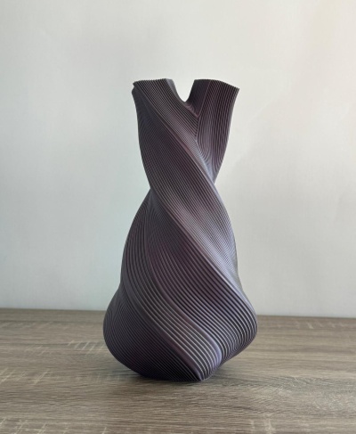 Vaso decorativo preto com textura em linhas torcidas sobre superfície de madeira.