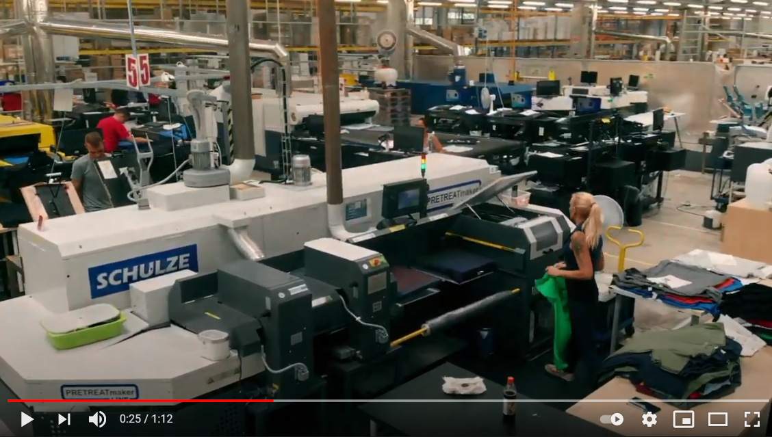 Fábrica com maquinaria industrial SCHULZE e mulher a manusear tecido verde em ambiente industrial têxtil