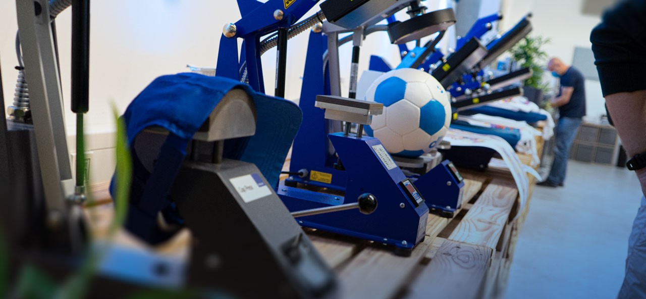 Máquinas de impressão térmica com bolas de futebol e bonés azuis num espaço interior