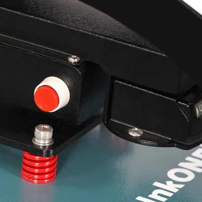Detalhe de máquina preta com botão vermelho e branco e superfície azul com texto parcial em branco