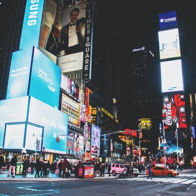 Rua comercial iluminada à noite com painéis luminosos e anúncios