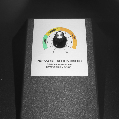 Botão de ajuste de pressão preto num painel metálico com escala colorida e texto de instrução.