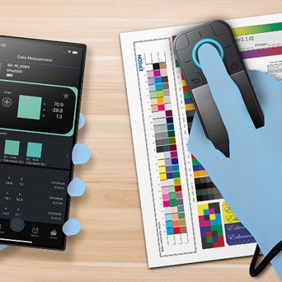 Dispositivo de medição de cor e smartphone em mãos com luvas azuis sobre mesa de madeira