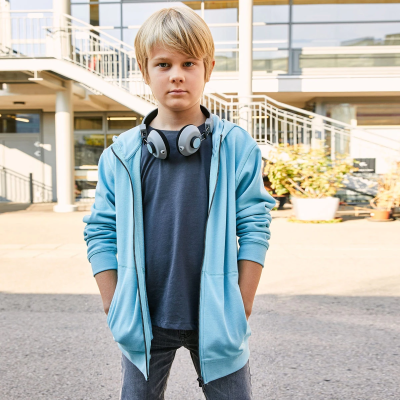 Rapaz com hoodie azul claro, t-shirt azul escura, jeans cinza e headphones cinzentos ao pescoço em ambiente exterior.
