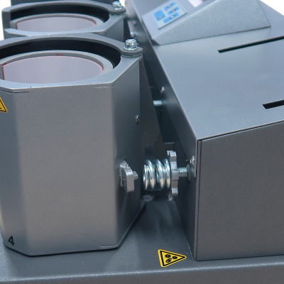 Máquina industrial cinza com roldanas e molas, com etiquetas de aviso amarelas