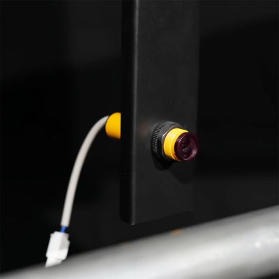 Sensor cilíndrico amarelo com cabo elétrico branco instalado em superfície preta