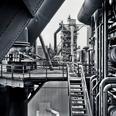 Estrutura industrial metálica com tubos e escadas em tons de cinza e preto