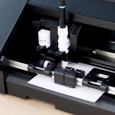 Impressora preta com caneta branca e componentes mecânicos expostos