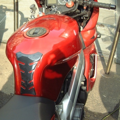 Motocicleta desportiva vermelha com depósito e assento preto, estacionada ao ar livre