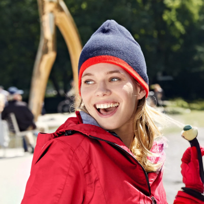 Mulher sorridente com gorro azul e vermelho e casaco vermelho no exterior