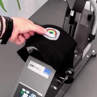Prensa térmica aplicando estampa arco-íris numa boné preto e texto MADE IN EUROPE.