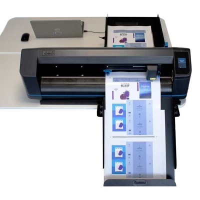 Impressora de grande formato Summit a imprimir folhas coloridas numa mesa branca com computador portátil