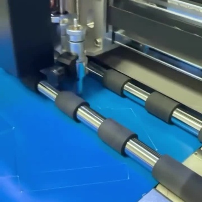 Máquina a recortar material azul e mãos a dobrar peça recortada
