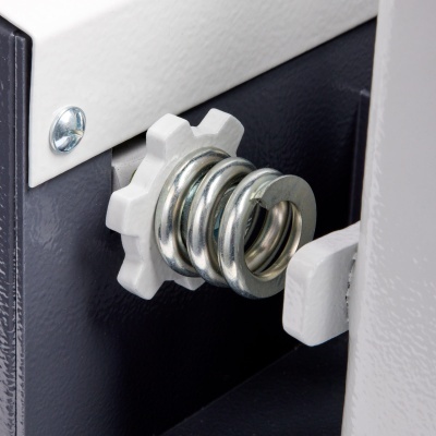 Mola metálica helicoidal prateada ligada a peça branca em formato de engrenagem numa estrutura metálica preta e cinza