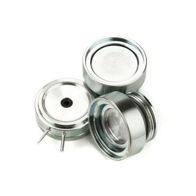 Três cápsulas metálicas prateadas com tampas, uma com tampa transparente, sobre fundo branco