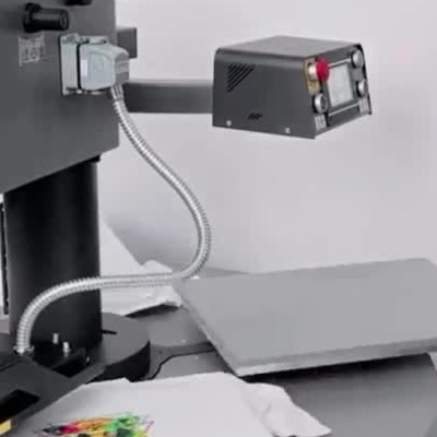 Máquina a imprimir desenhos coloridos em t-shirts brancas numa prensa térmica.