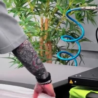 Máquina de impressão térmica com t-shirt e botões de controlo num ambiente com plantas.