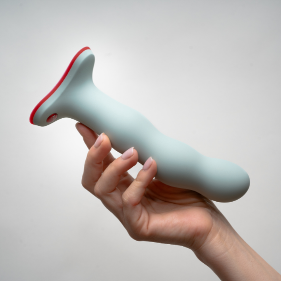 Dildo com vibração manual 100% silicone soft touch | Bouncer Fun Factory Objeto cilíndrico azul claro com base vermelha segurado por uma mão, textura lisa, fundo branco.