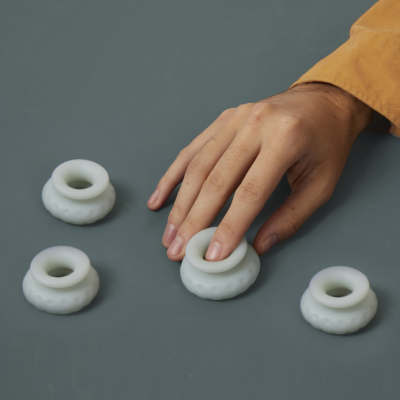Anéis de silicone brancos com textura circular e uma mão sobre uma superfície cinza