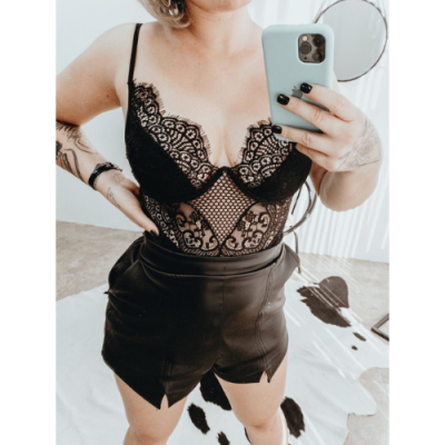 Mulher com body de renda preto e saia de couro preto tirando selfie em ambiente interior