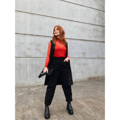 Mulher com roupa preta e vermelha posando em frente a parede cinza