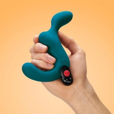 Dispositivo sexual verde em silicone com controle remoto, em fundo laranja.