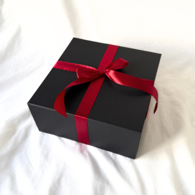 Caixa preta com fita vermelha sobre tecido branco