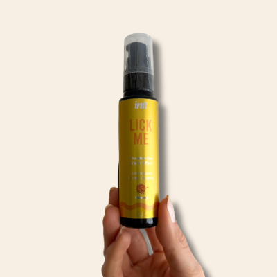 Frasco amarelo com tampa preta e texto LICK ME, segurado por uma mão