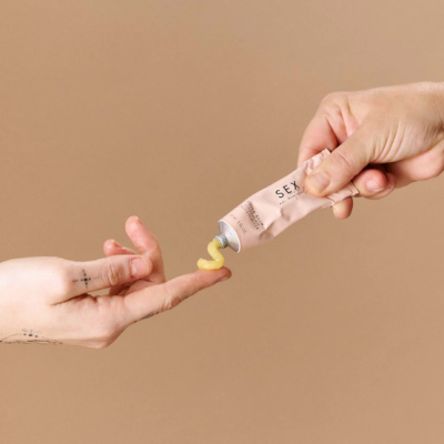 Aplicação de gel amarelo de tubo rosa com texto SEX nas mãos sobre fundo castanho