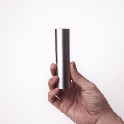 Frasco cilíndrico prateado metálico segurado por mão com fundo branco