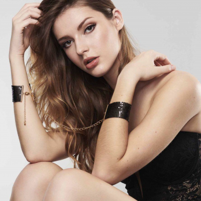 Mulher com pulsoiras pretas ligadas por corrente dourada num fundo branco