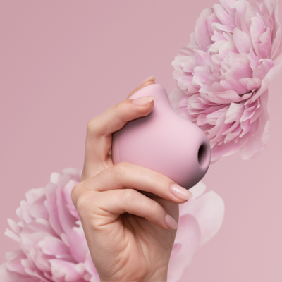 Objeto rosa claro arredondado com orifício segurado por mão contra fundo rosa com flores