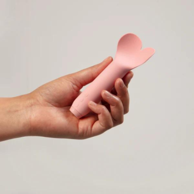 Objeto rosa de silicone semelhante a uma pétala segurado por uma mão sobre fundo cinzento.