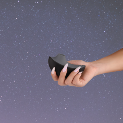 Mão com unhas compridas a segurar dispositivo preto curvo sobre fundo estrelado