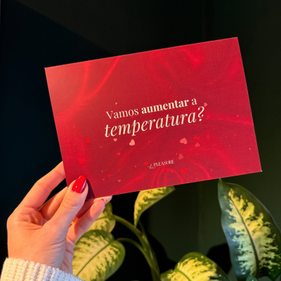 Cartão vermelho com texto em português segurado por uma mão, plantas ao fundo.