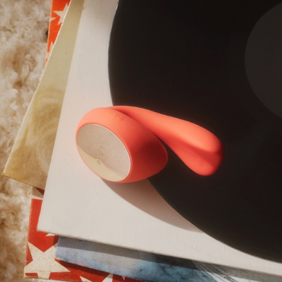 Dispositivo laranja com base metálica prateada LELO em cima de discos de vinil