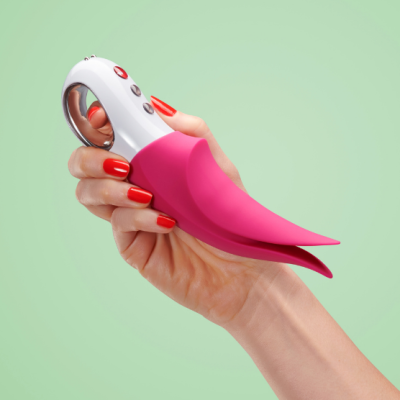 Dispositivo portátil rosa e branco com botões, segurado por mão com unhas vermelhas, fundo verde claro