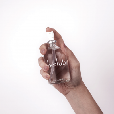 Mão segurando frasco transparente de spray berlub com fundo branco